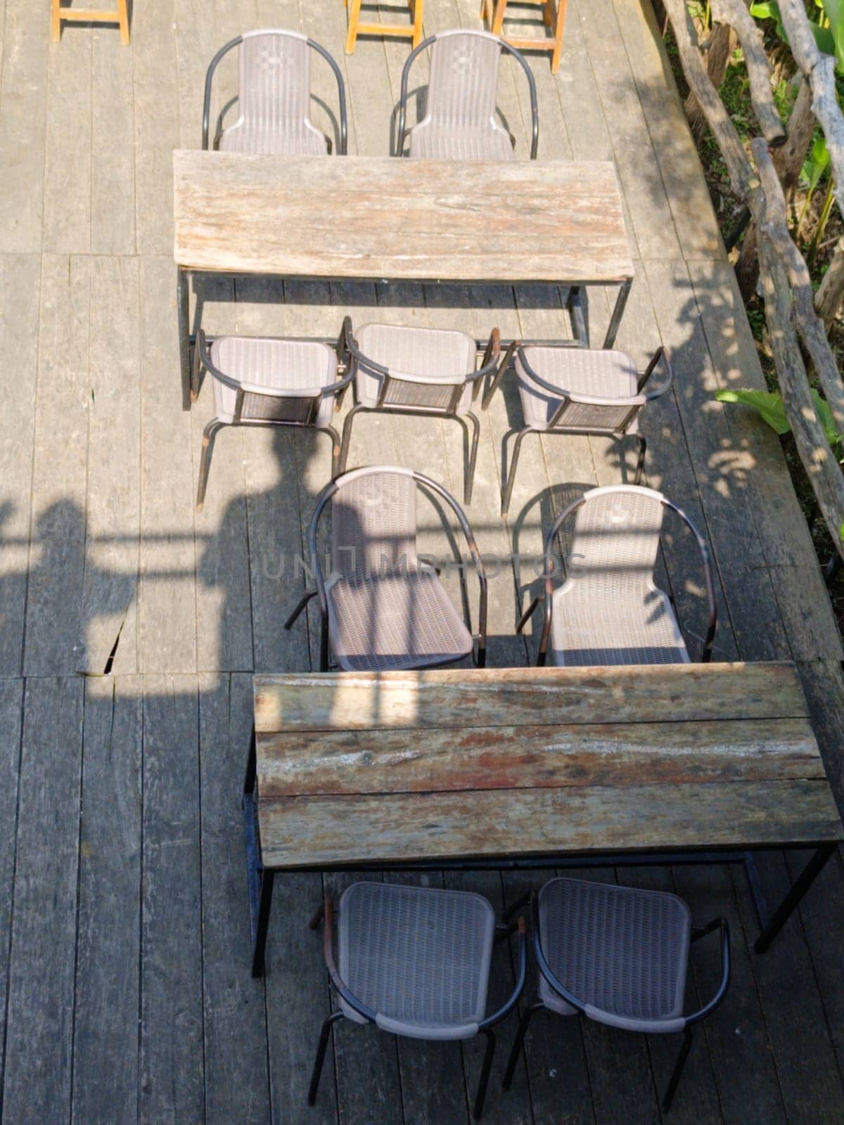 Top view of empty rustic wooden tables with chairs on an outdoor wooden deck, creating a serene and inviting atmosphere. There is also shadows of people from a rooftop
