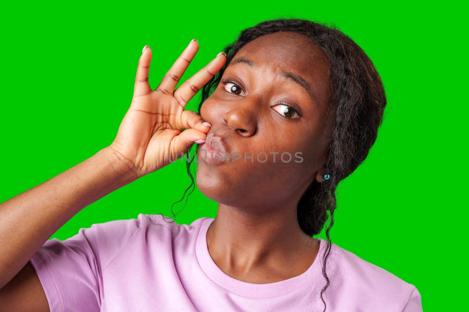 A young woman in a pink shirt makes a shushing gesture against a bright green background in studio