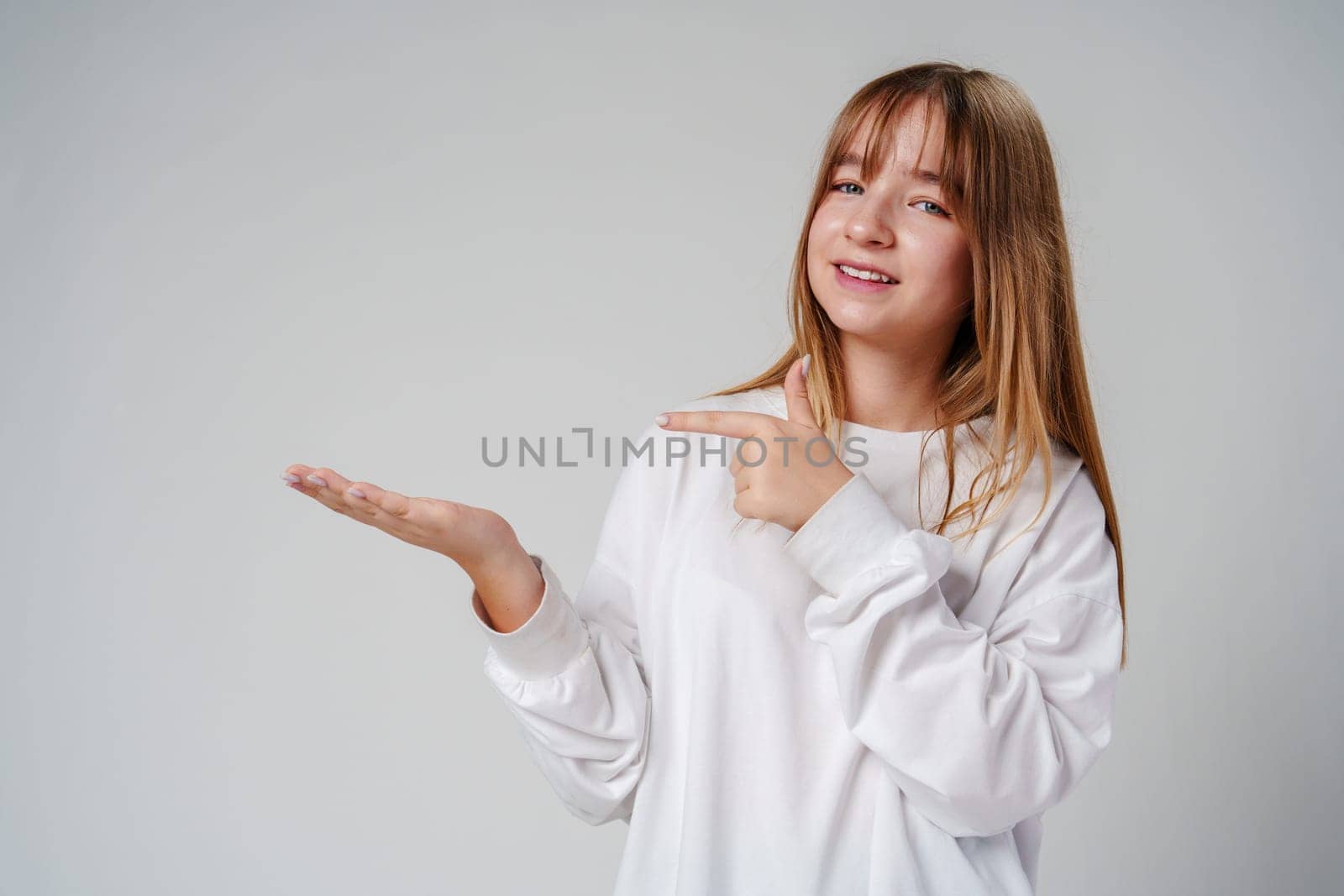 Young girl happily pointing against a neutral background while wearing a cozy white sweatshirt close up