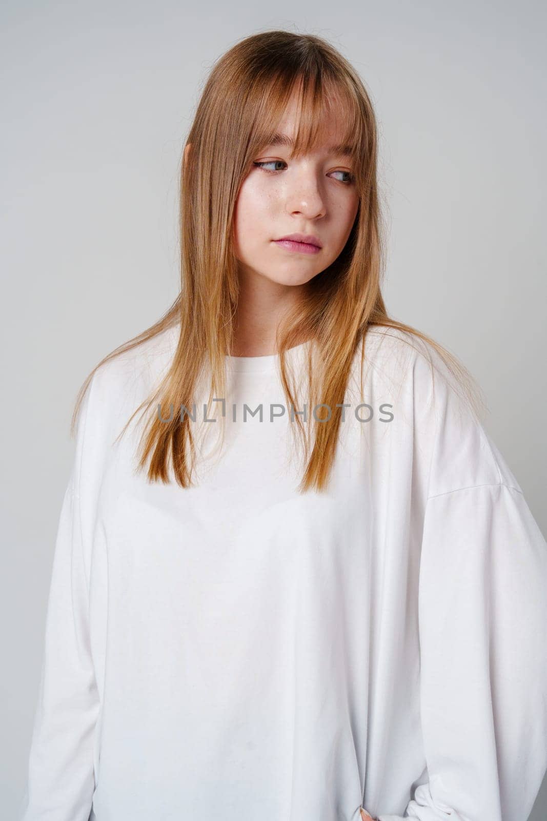 Casual portrait of a young girl wearing a white long-sleeve shirt and blue jeans in a minimalist studio close up