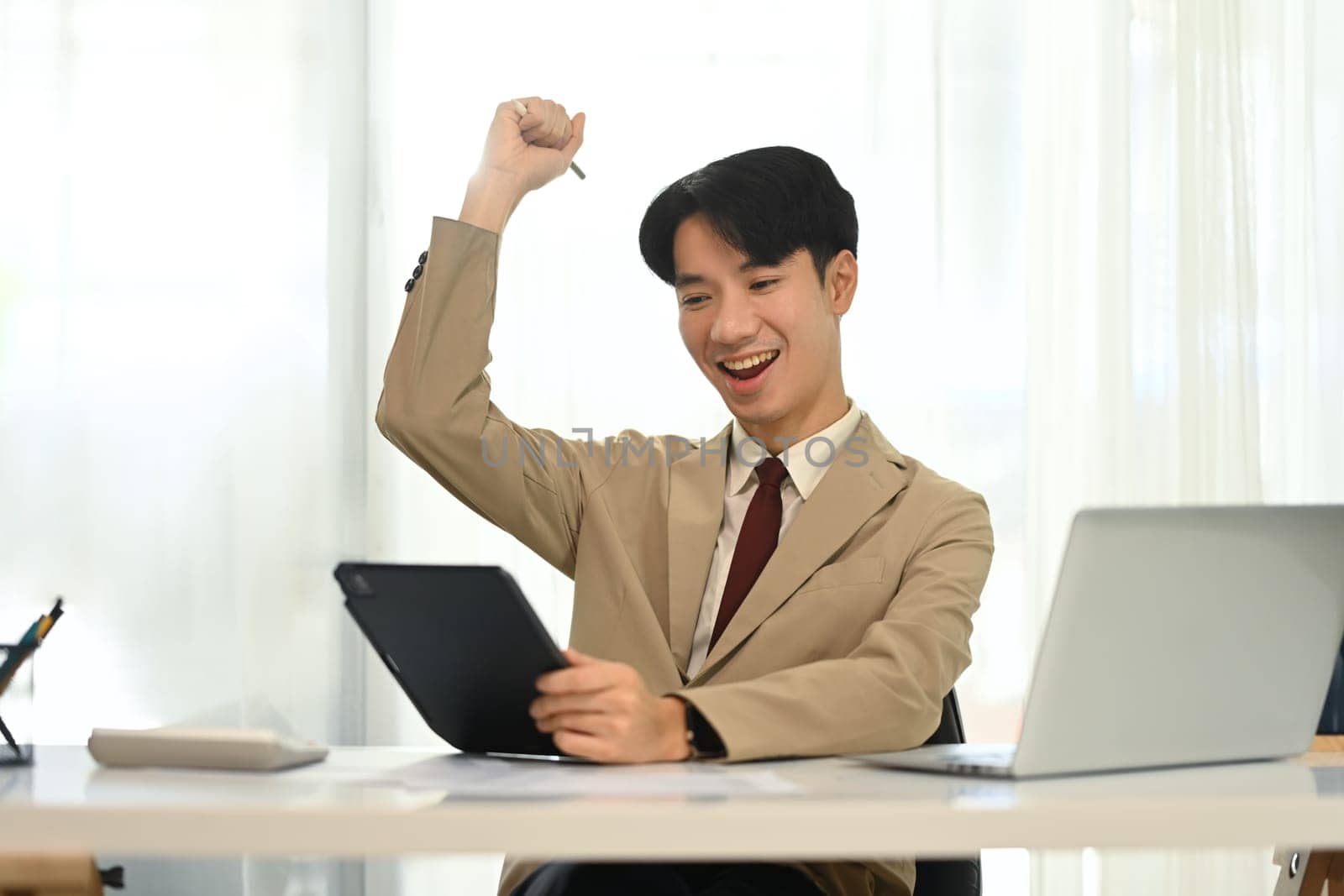 Excited businessman celebrating success while using tablet at work.