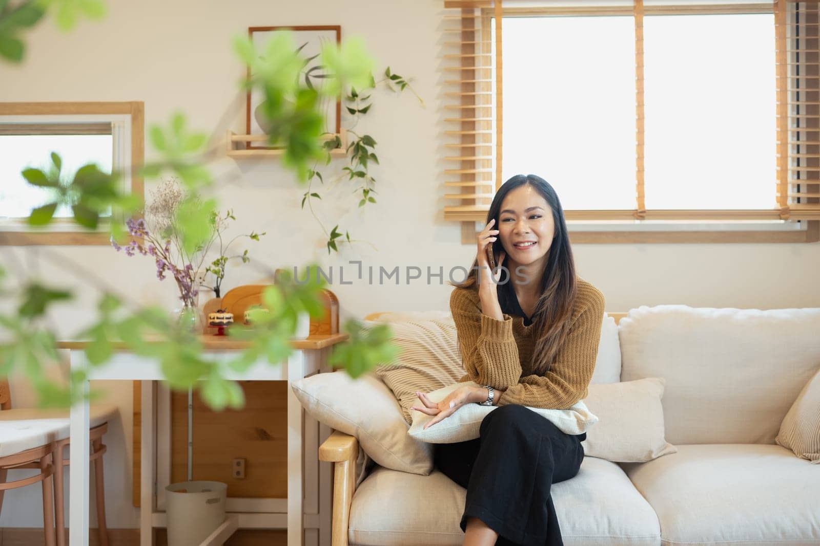 Beautiful young Asian woman talking on mobile phone in her living room.