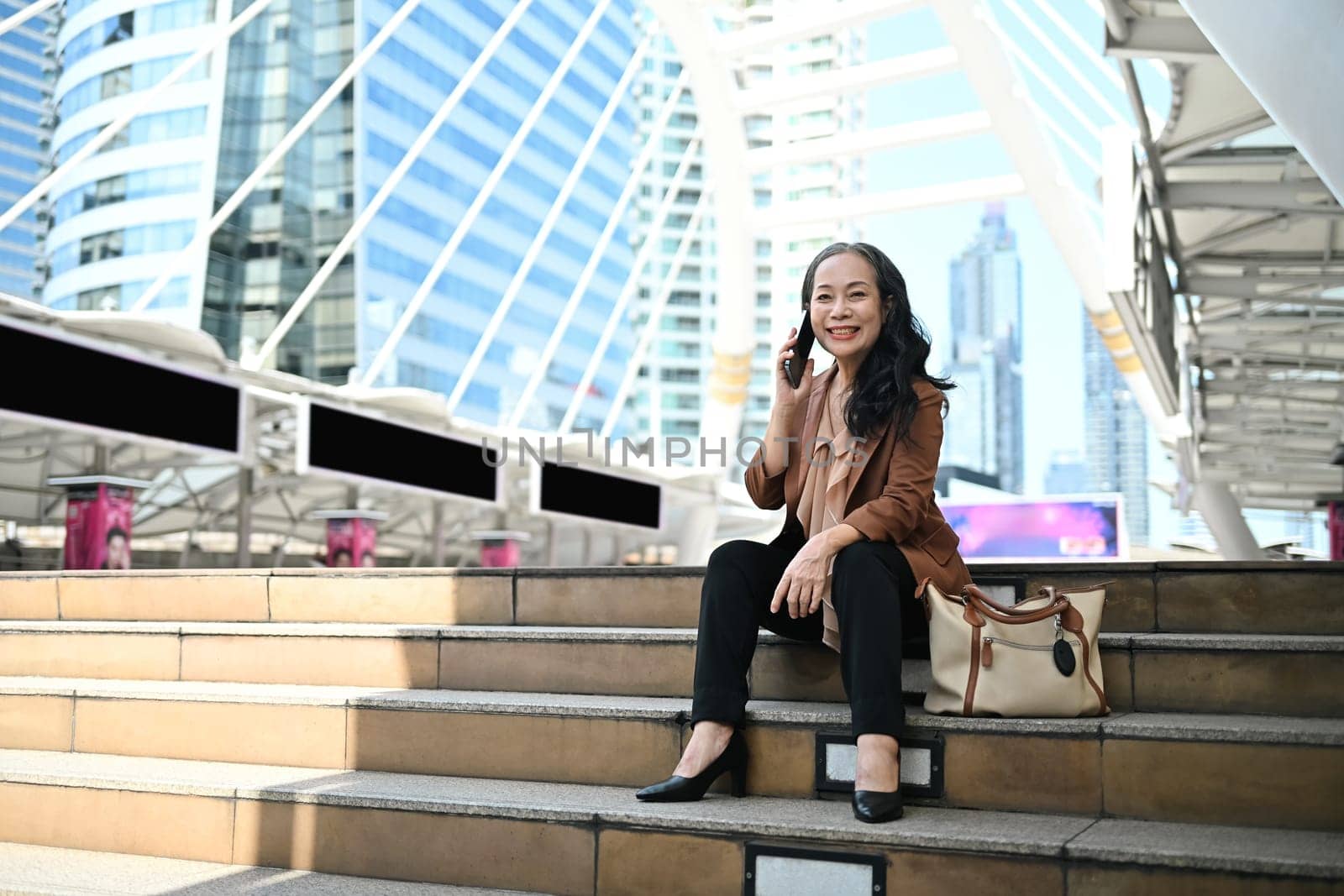 Confident mature businesswoman enjoying a phone conversation in modern city.
