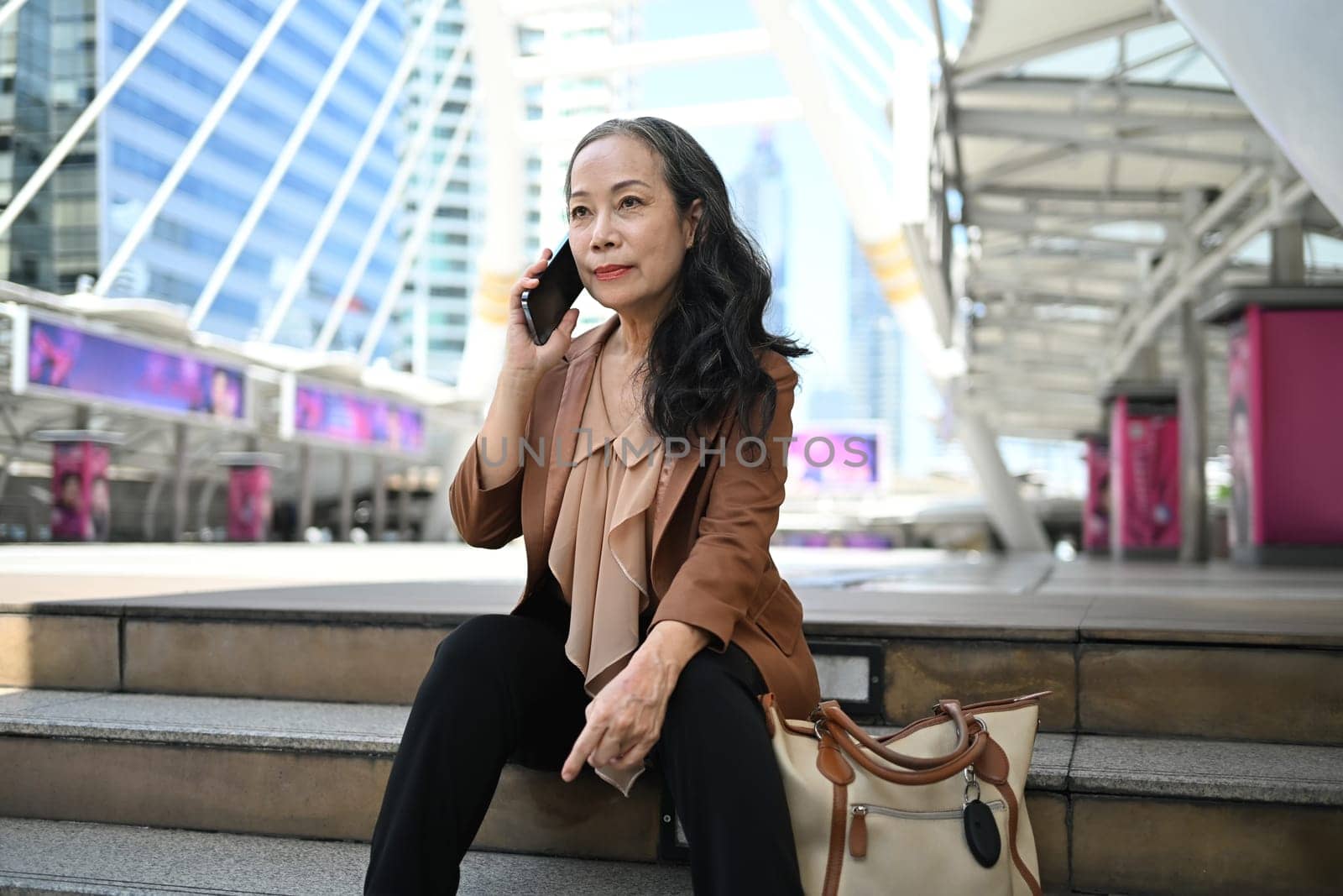 Confident mature businesswoman enjoying a phone conversation in modern city.