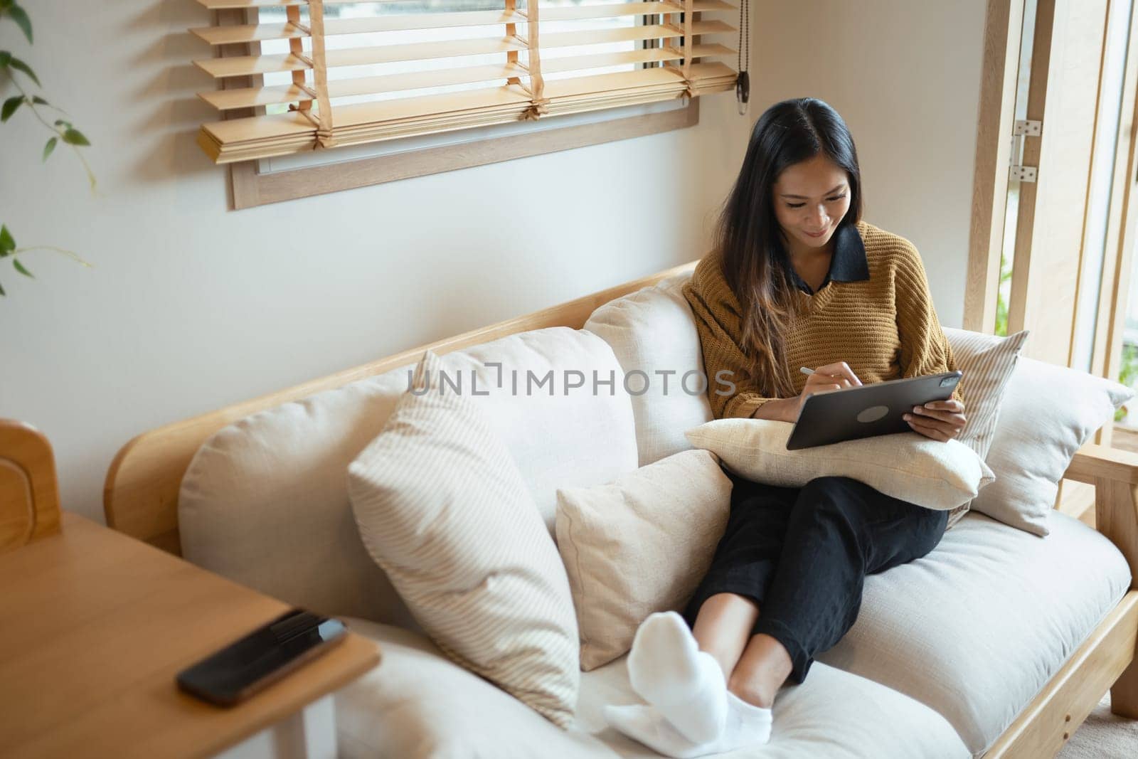 Smiling young woman using digital tablet in living room.
