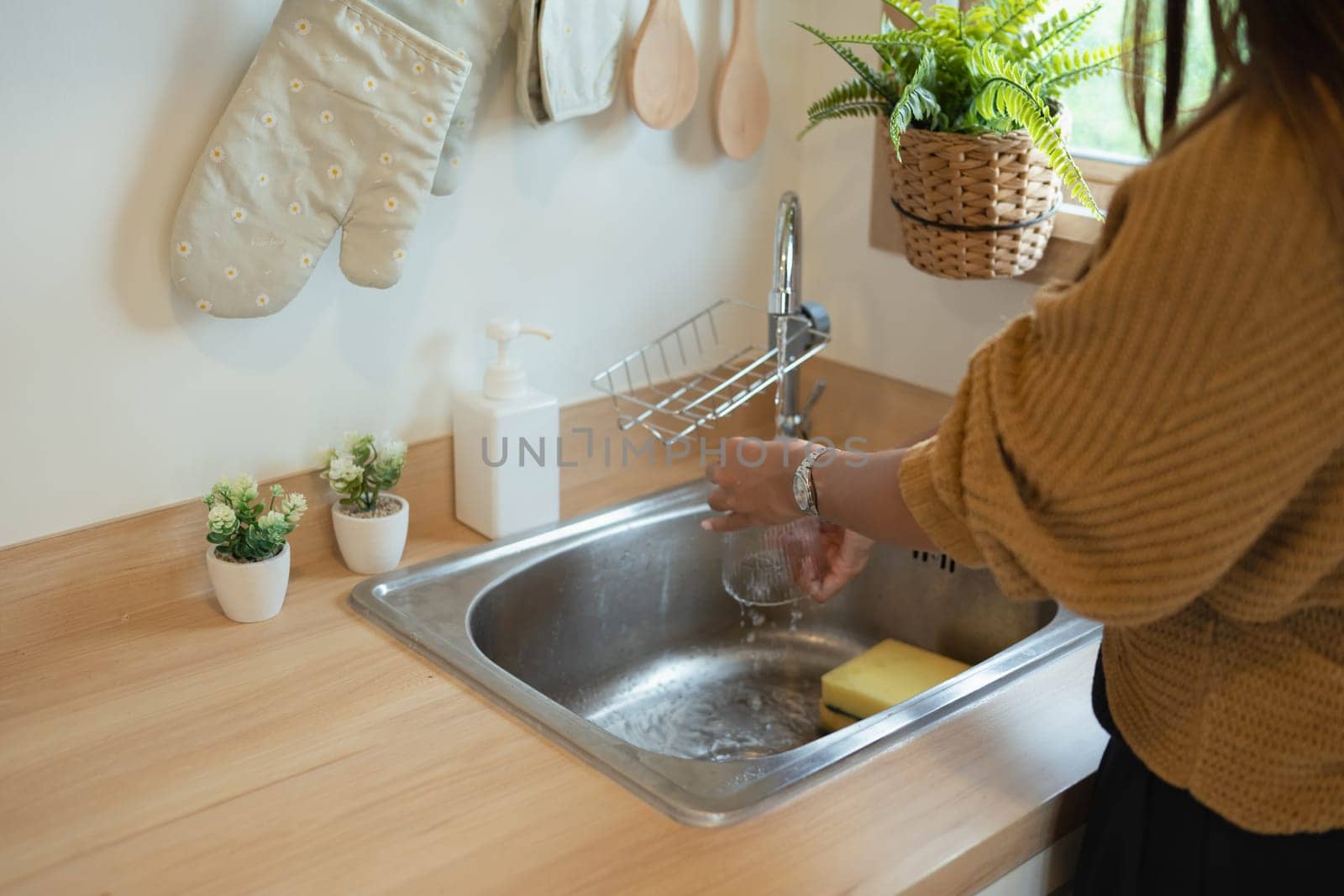 Young woman washing glass in kitchen sink.