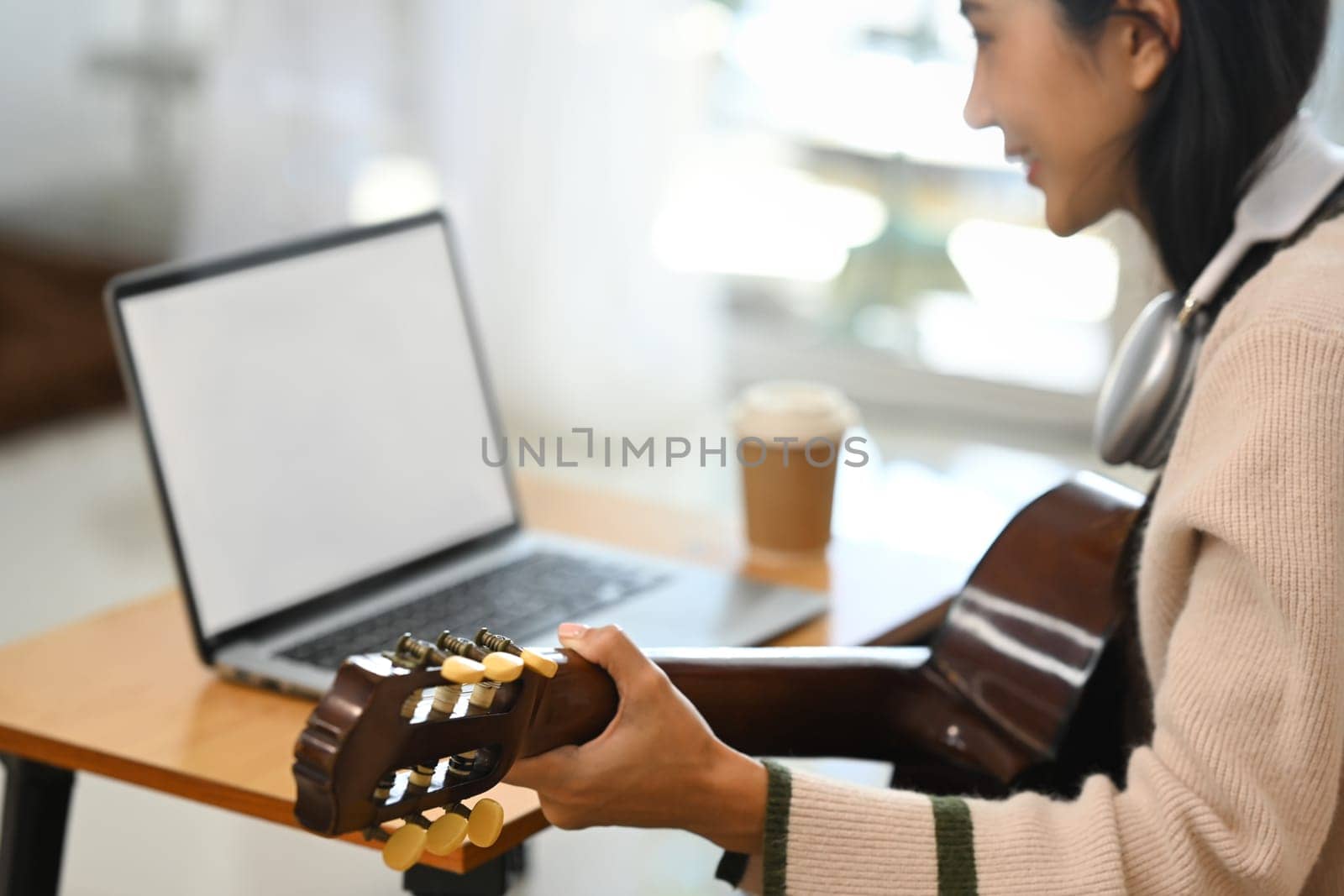 Young woman playing guitar while following online course on laptop.