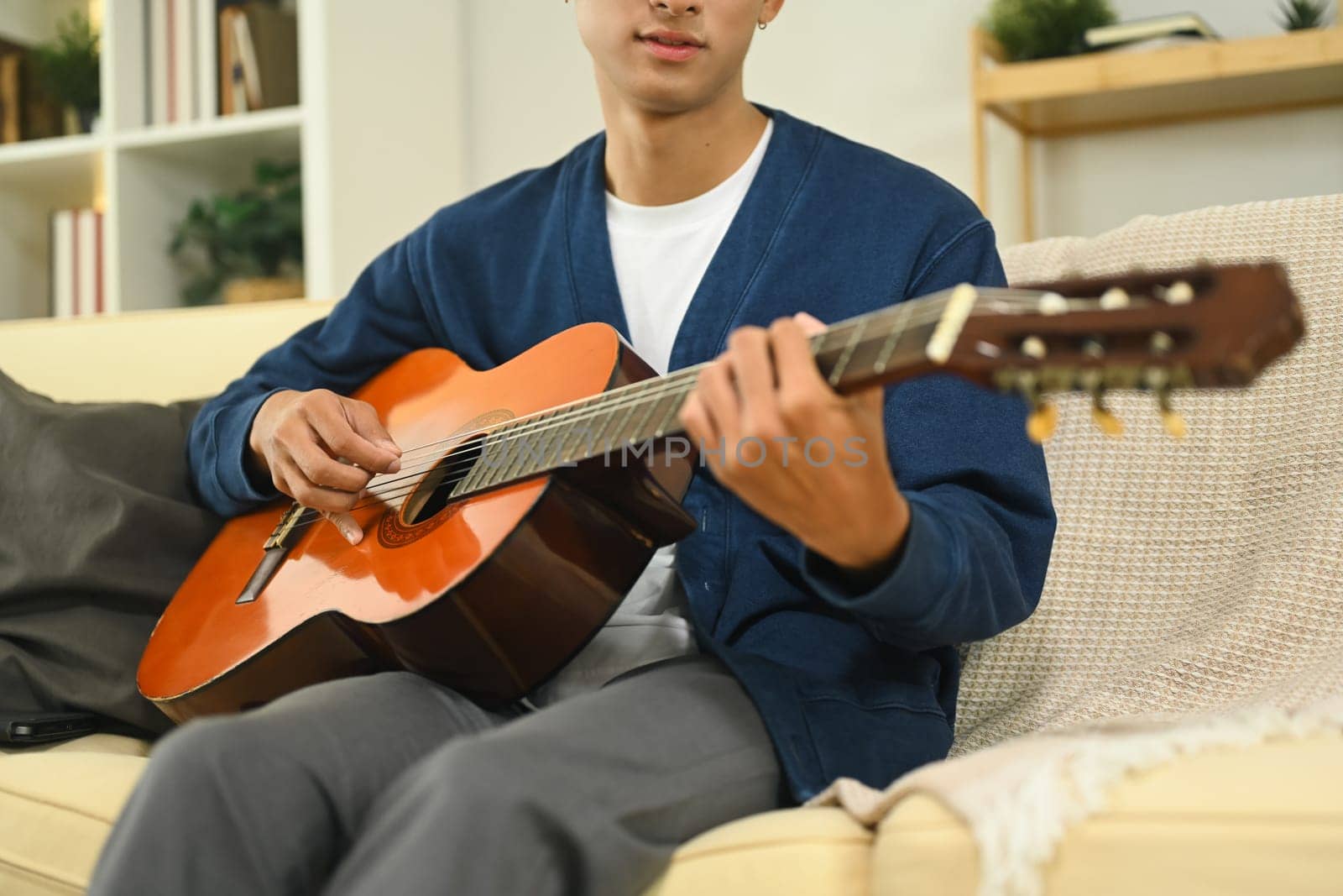Young asian man practicing acoustic guitar in a cozy living room.