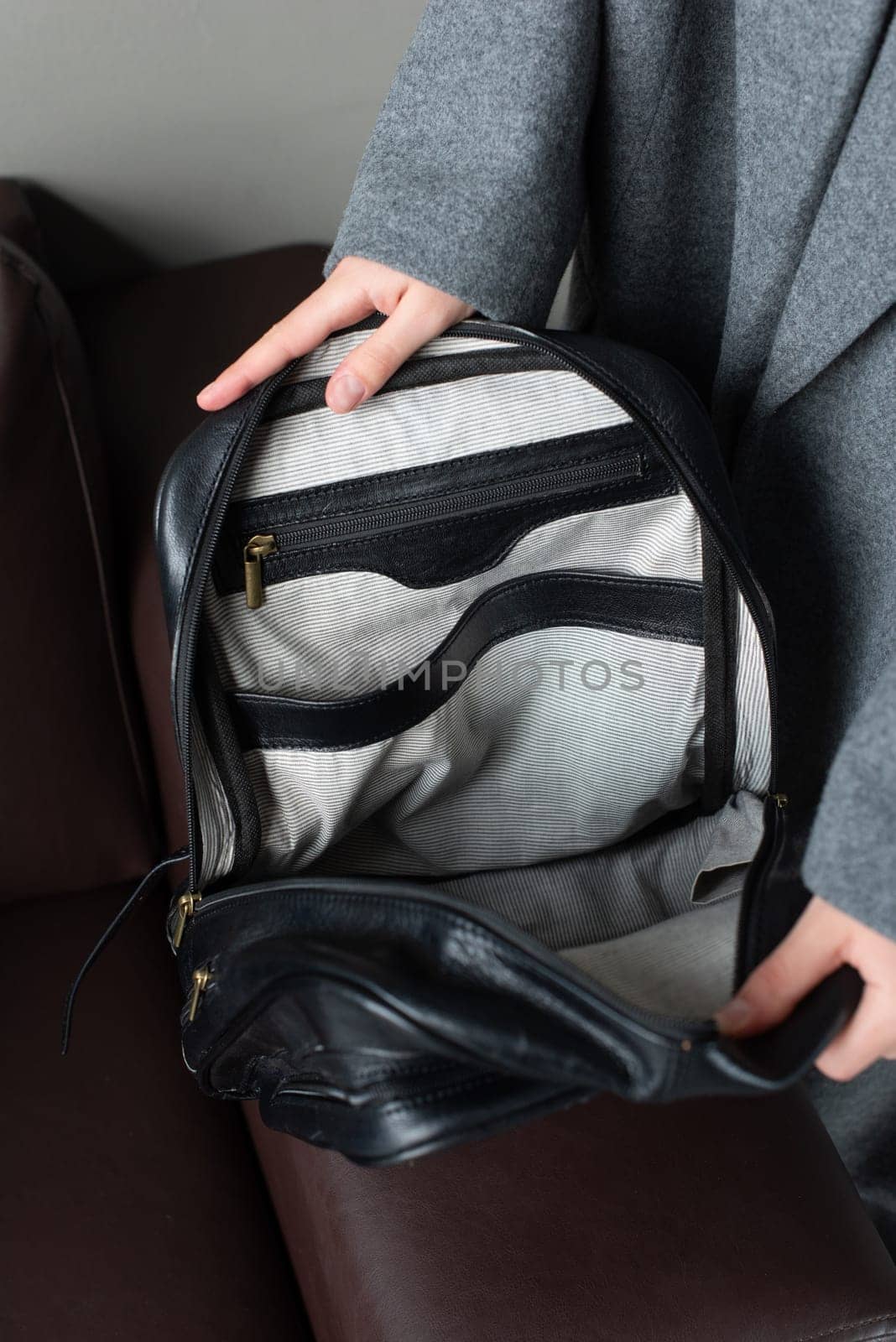 woman holds a black leather backpack. open, empty bag.