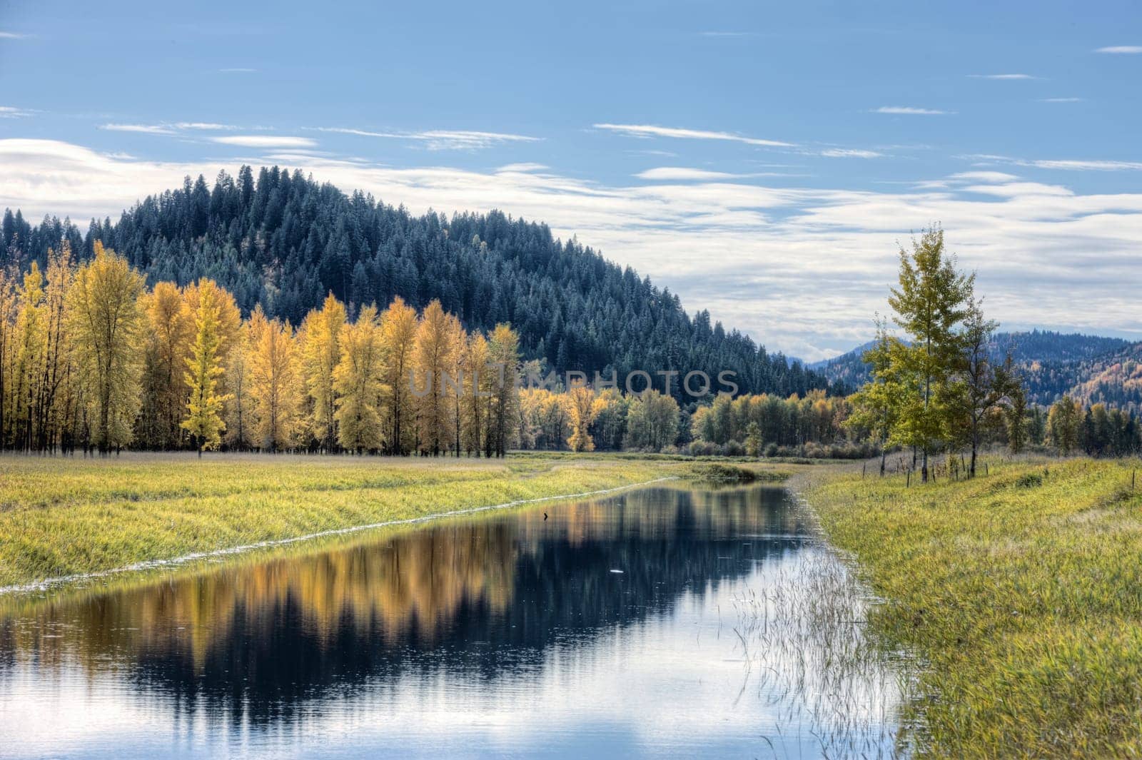 Calm water of the canal reflects the clouds in the partly blue sky on an autumn day near Bonners Ferry, Idaho.