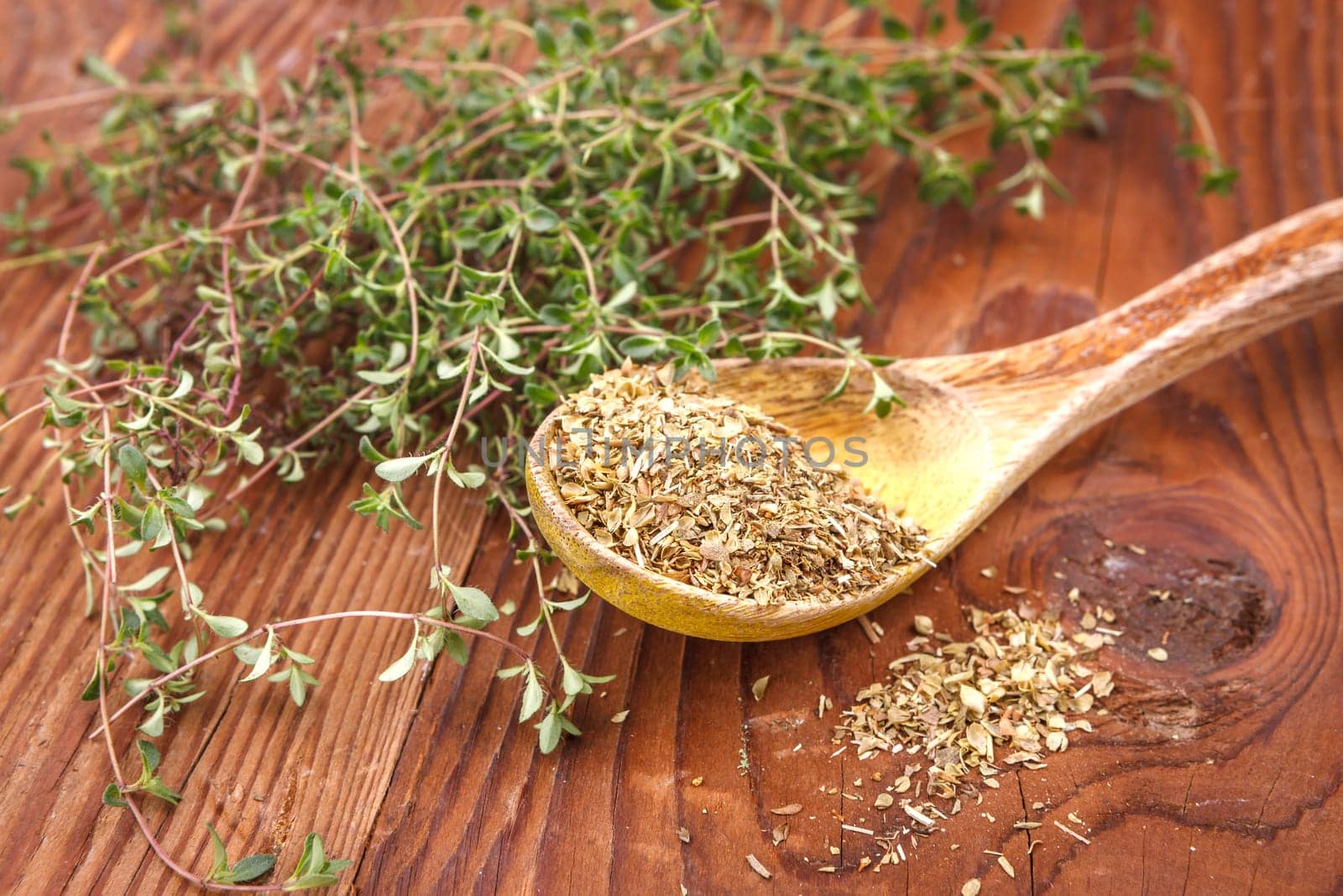 Display of dried thyme leaves on a spoon surrounded by fresh thyme leaves.