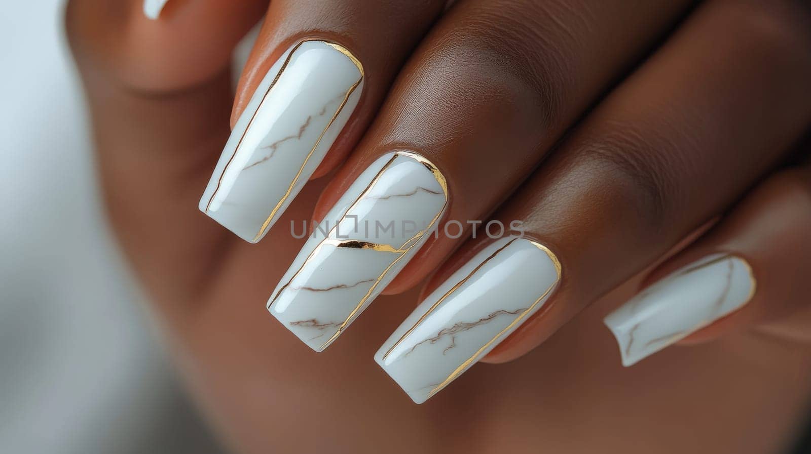 Luxurious close-up of a woman's hand showcasing an exquisite manicure. the nails feature a white marble design highlighted with gold accents, reflecting elegance and high fashion in beauty trends.