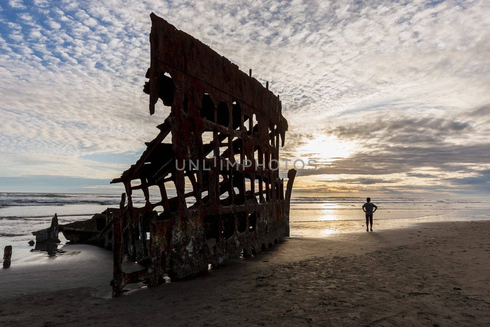 Boy stands by the Peter Iredale shipwreck at sunset in Oregon.