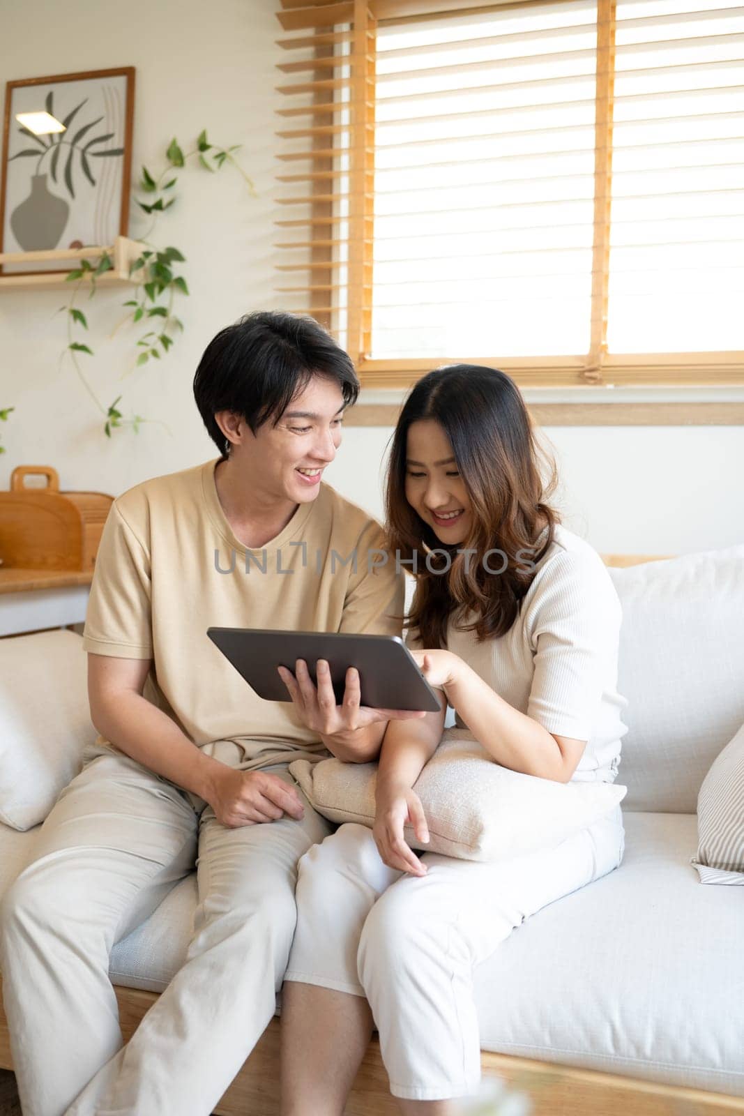 Smiling young couple relaxing with digital tablet on couch at home.