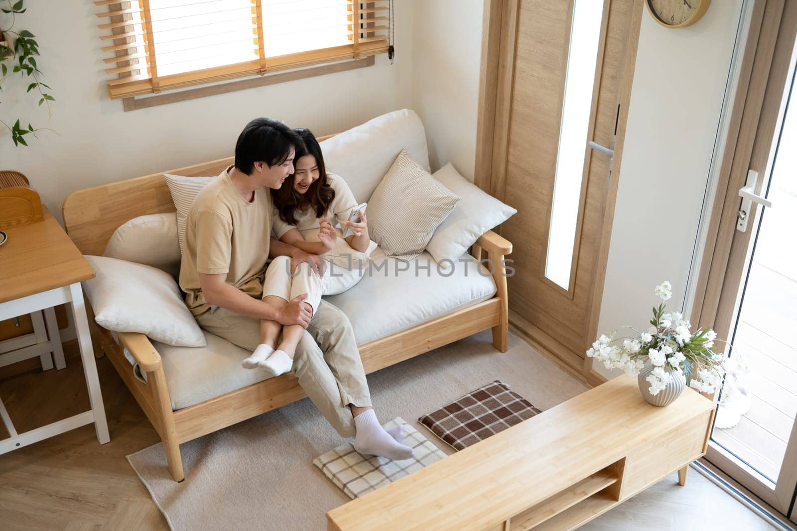 Loving asian couple sharing a cozy moment while browsing on smartphone at home.