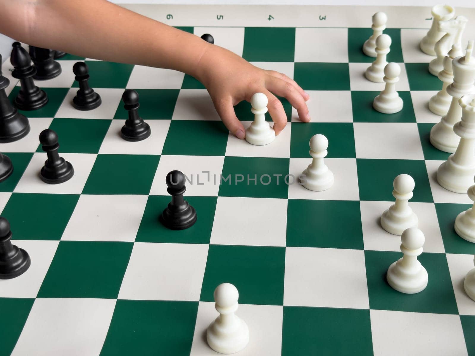 Childs hand moving chess piece on green and white chessboard with black and white pieces.