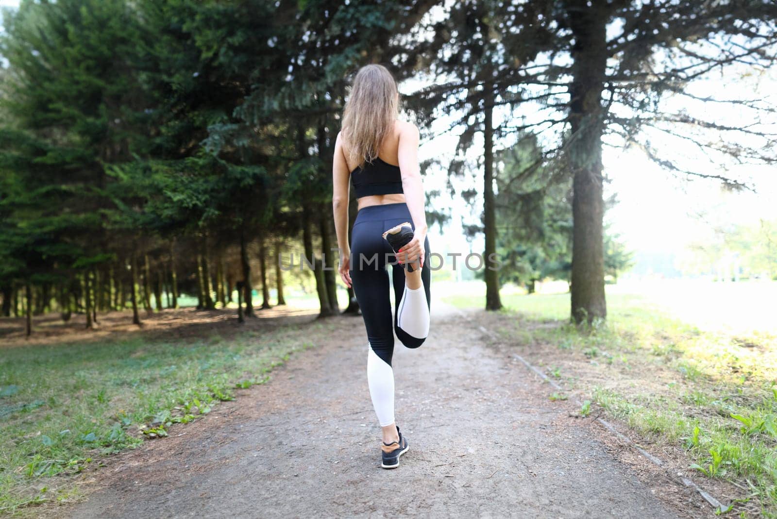 Close-up of sporty young woman training in summer forest. Fit and strong female doing exercise far away from people. Lady in trendy comfy sportswear. Sport and hobby concept