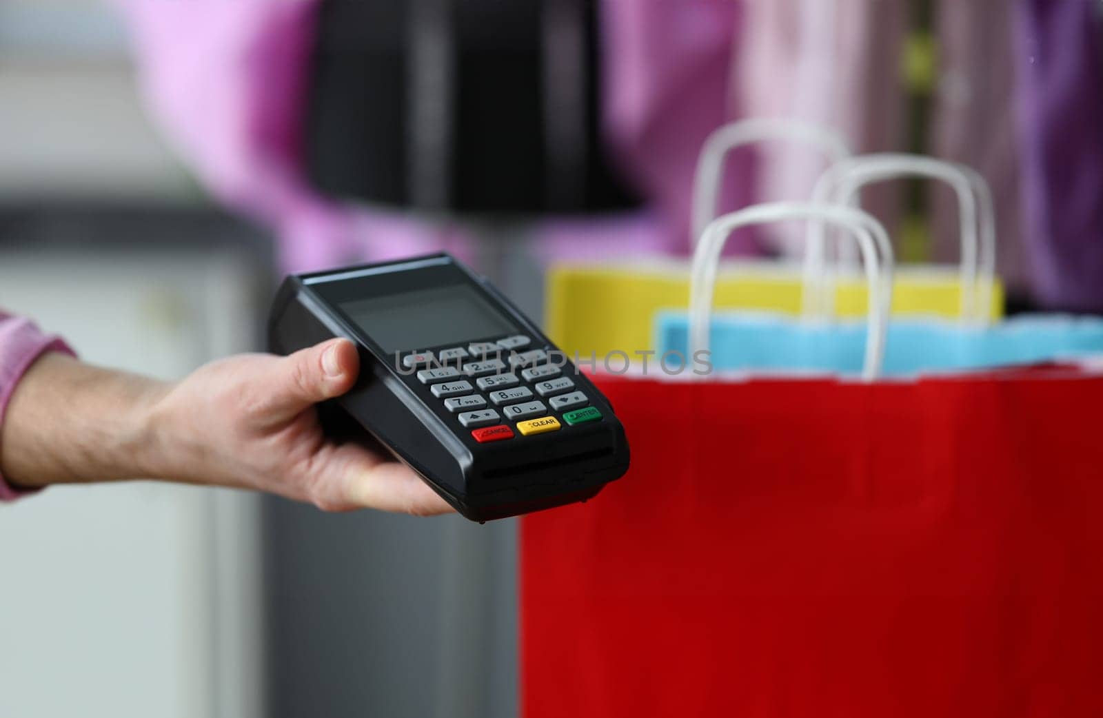 Close-up of person holding cashier machine for fast payment. Nfc technology counter. Colourful package with stuff. Online shopping and modern gadget concept
