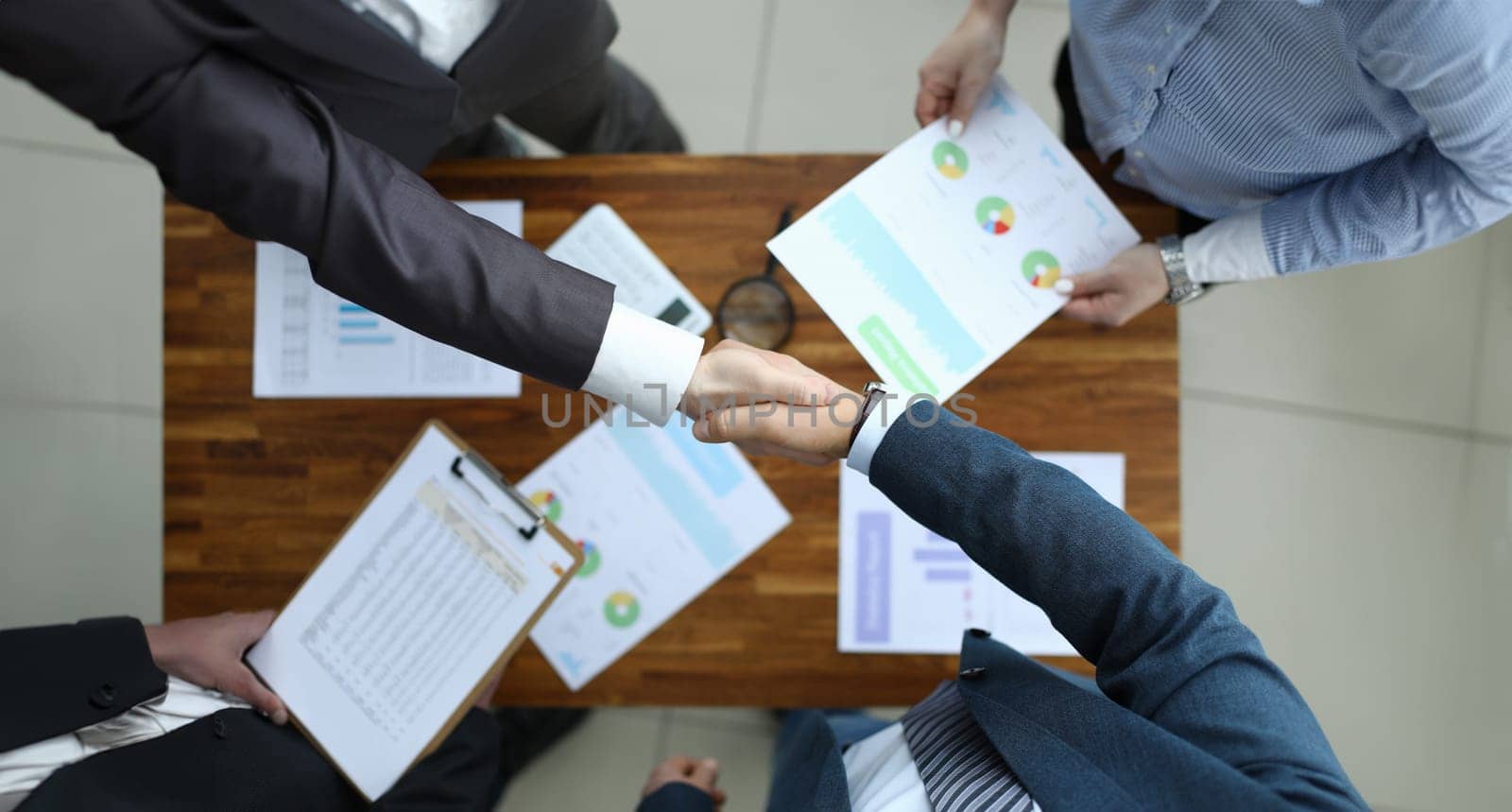 Top view of business team shaking hands. Conference room with executive manager accountant and employee. Good deal and financial report. Papers with charts on wooden table