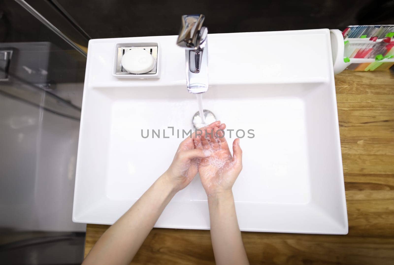 Top view of person washing hands with soap under water. Prevention infection spread. Clean white modern faucet. Silver crane. Bathroom and personal hygiene concept