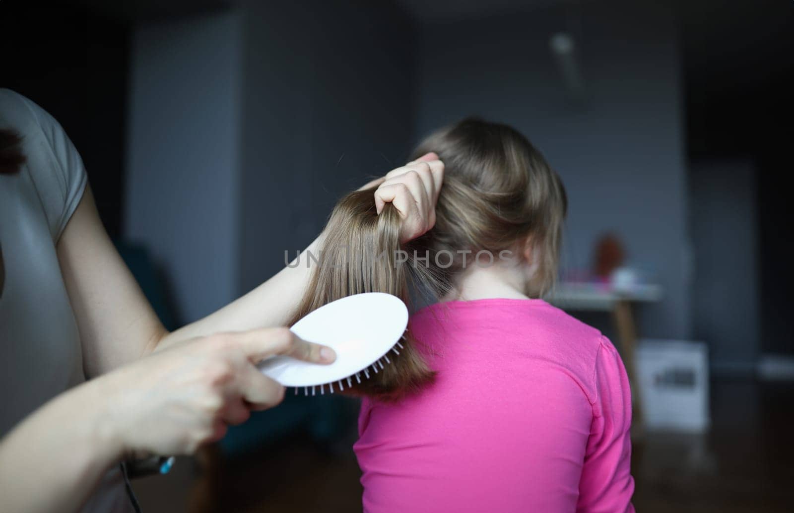 Close-up of mother brush daughter hair with wooden comb. Mum and child time together. Girl with beautiful hairstyle. Treatment before sleep. Daily routine and health concept
