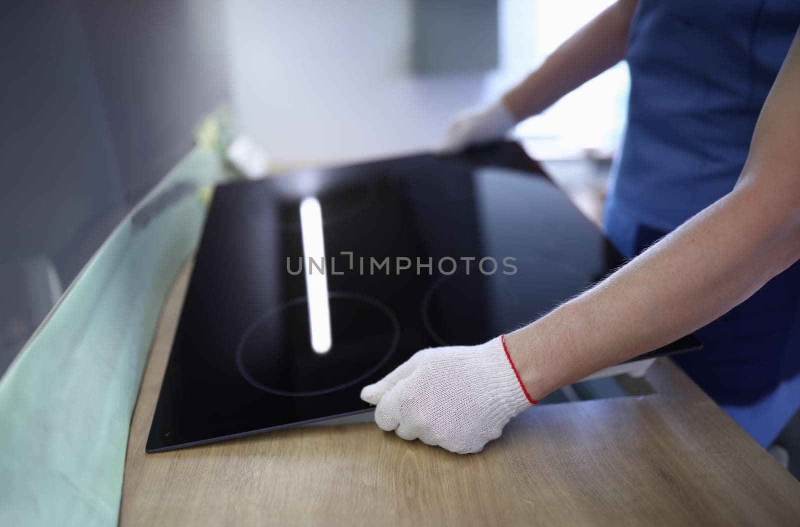 Close-up of professional worker setting cookstove in kitchen room. New modern cooker. Man wearing protective white gloves for work. Renovation and furniture change concept