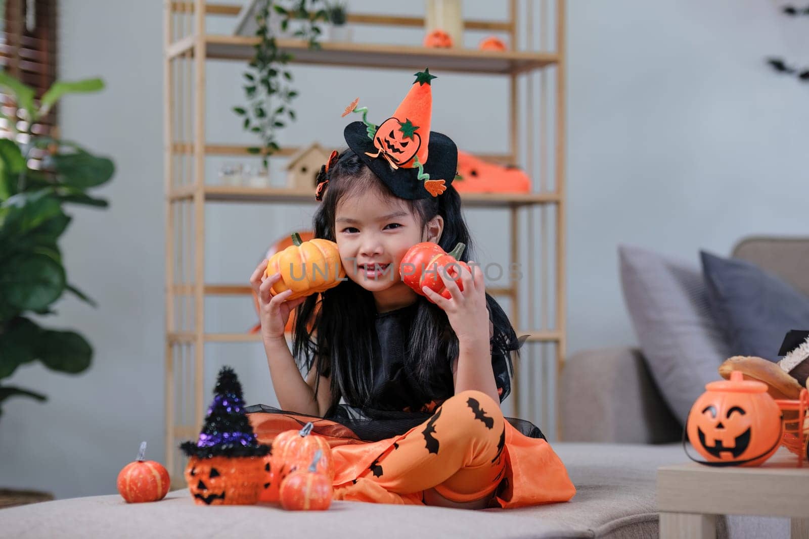 Cute little girl wearing a Halloween costume holding a pumpkin at home with happy eyes. looking at the camera..