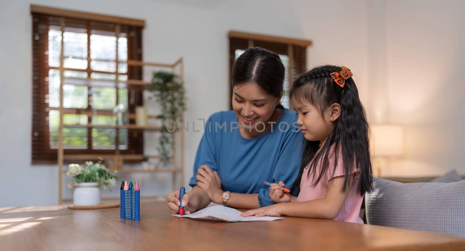 Happy family mother and daughter study or draw together at home in living room.