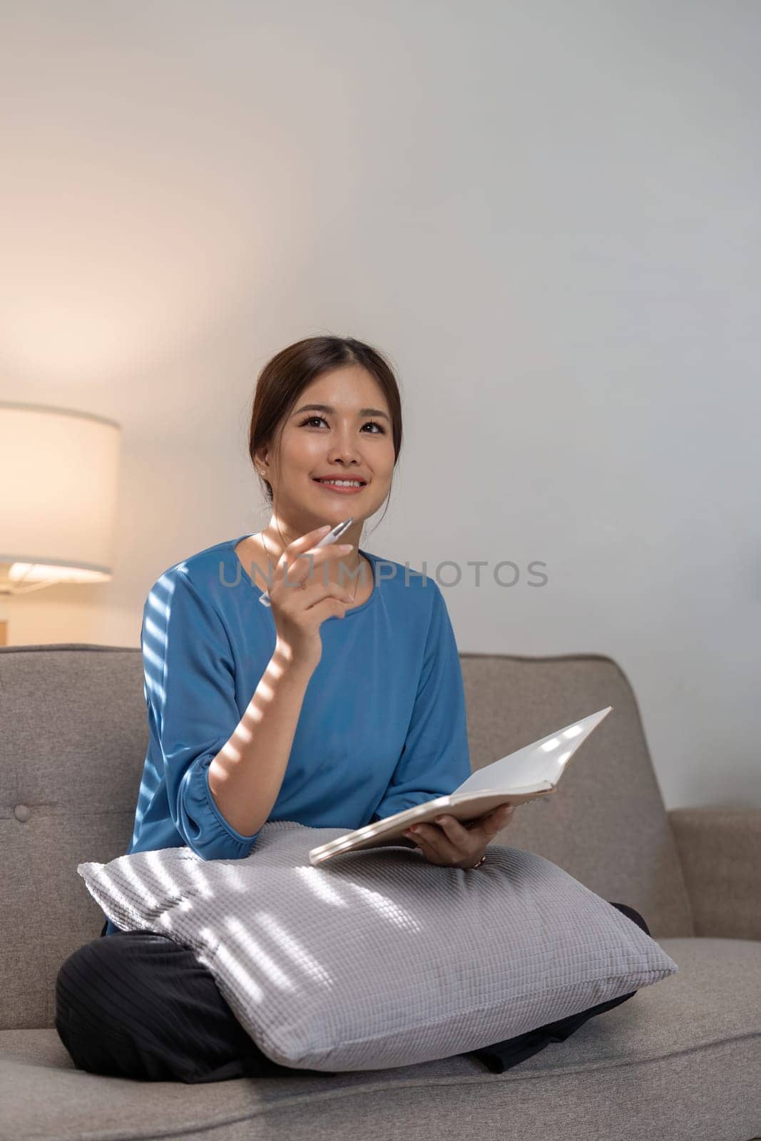 Beautiful young asian woman sitting and taking note on sofa at house. Happy smiling working online, Freelance work at home by nateemee
