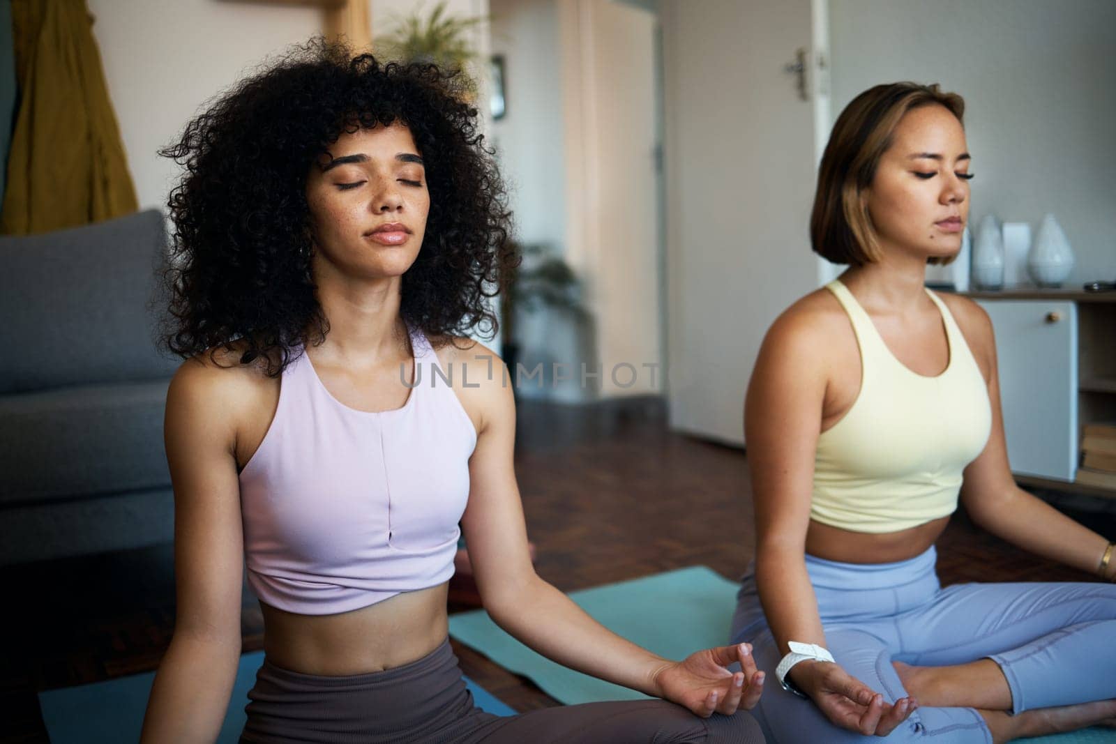 Meditation, yoga and girl friends in the living room doing fitness in lotus position together. Calm, peace and young women doing pilates workout or exercise for breathing in the lounge at home by YuriArcurs