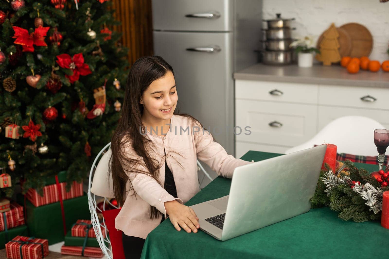 A girl during Christmas, sitting at home in the kitchen, congratulates her friends or grandparents via video communication by Andelov13