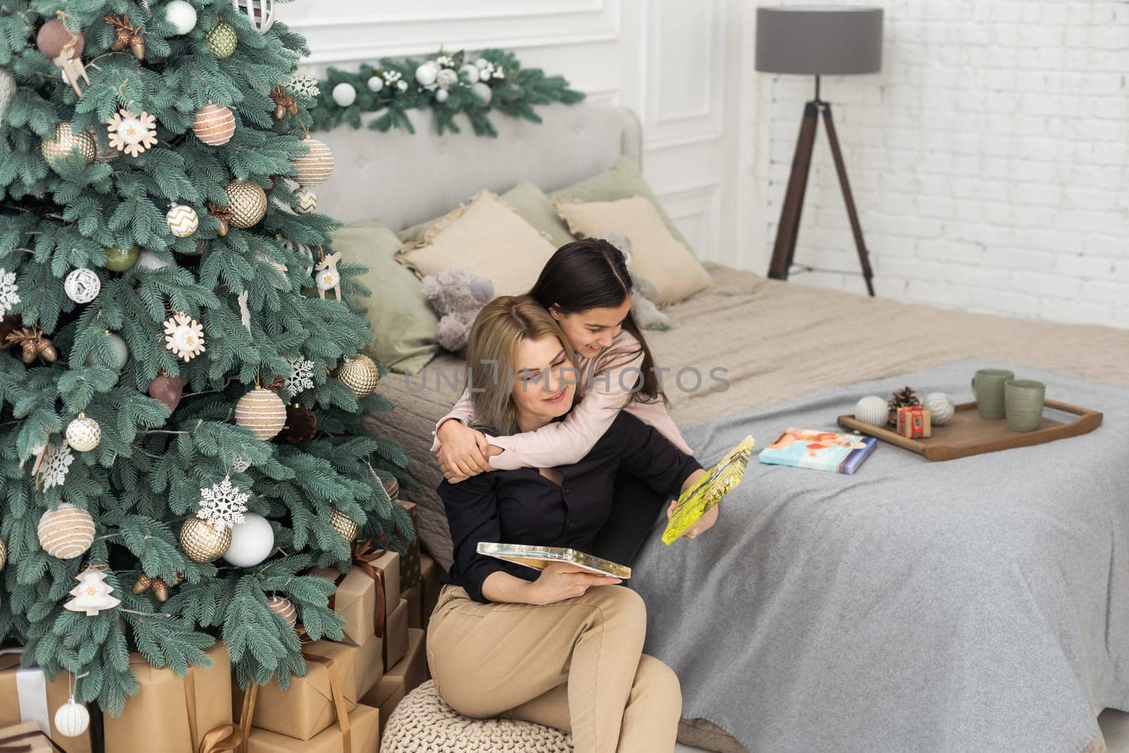 Beautiful young mother with long hair is reading a photo book with her little daughter. christmas home decor. warm tinted photo