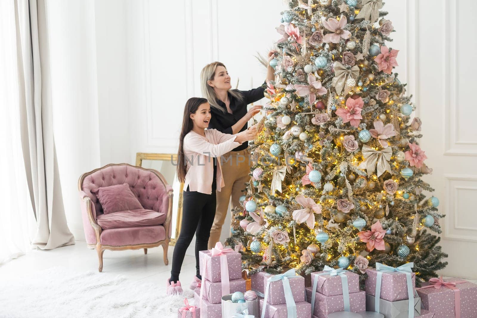 family, winter holidays and people concept - happy mother and little daughter decorating christmas tree at home