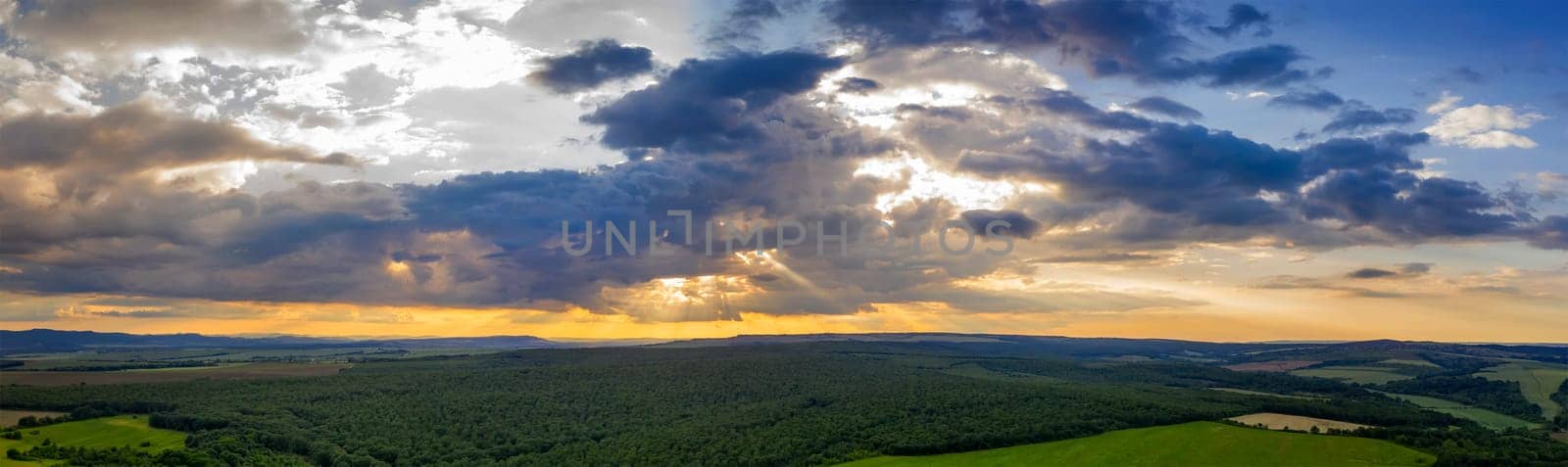 Panoramic Aerial View view of the countryside and cloudy sky with sun rays. Countryside covered with green forest.