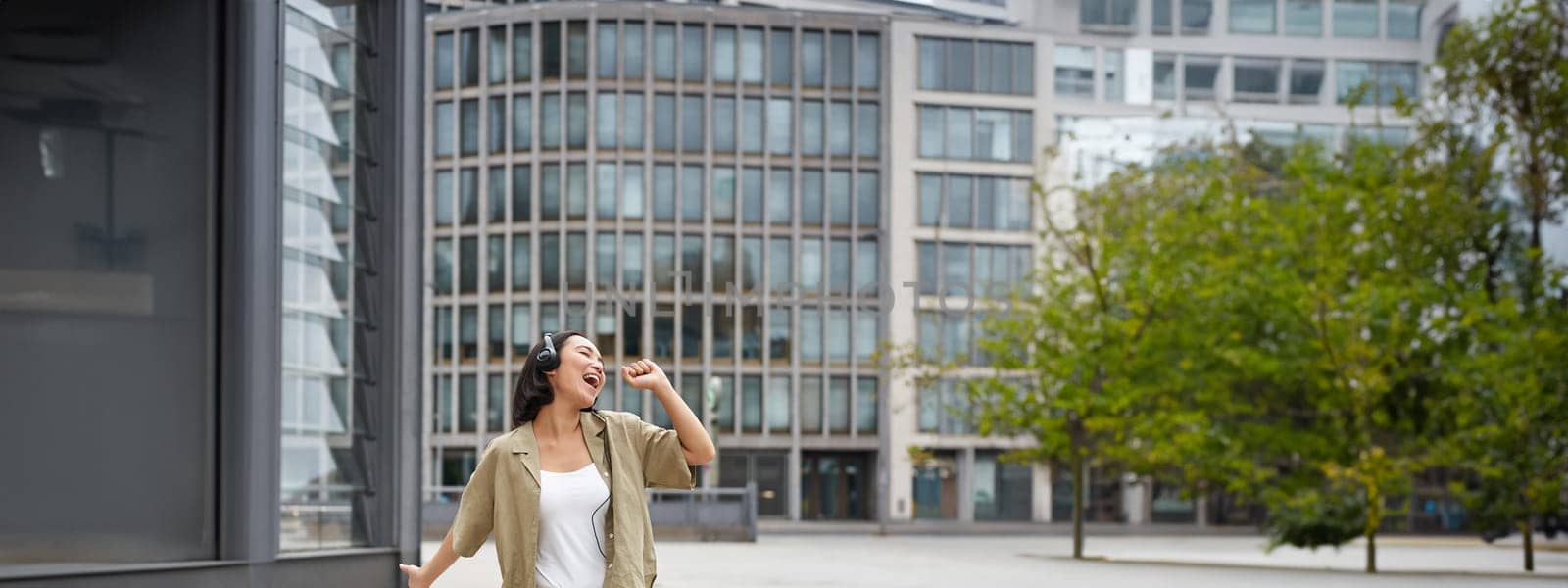 Happy people in city. Upbeat young girl dancing on street in headphones, listening music in headphones.