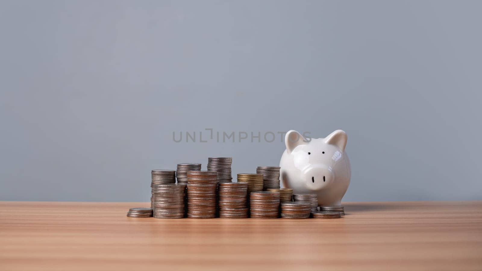 Piggy bank and coins lined up on a wooden floor with a white background. Concepts of finance, savings and investment.