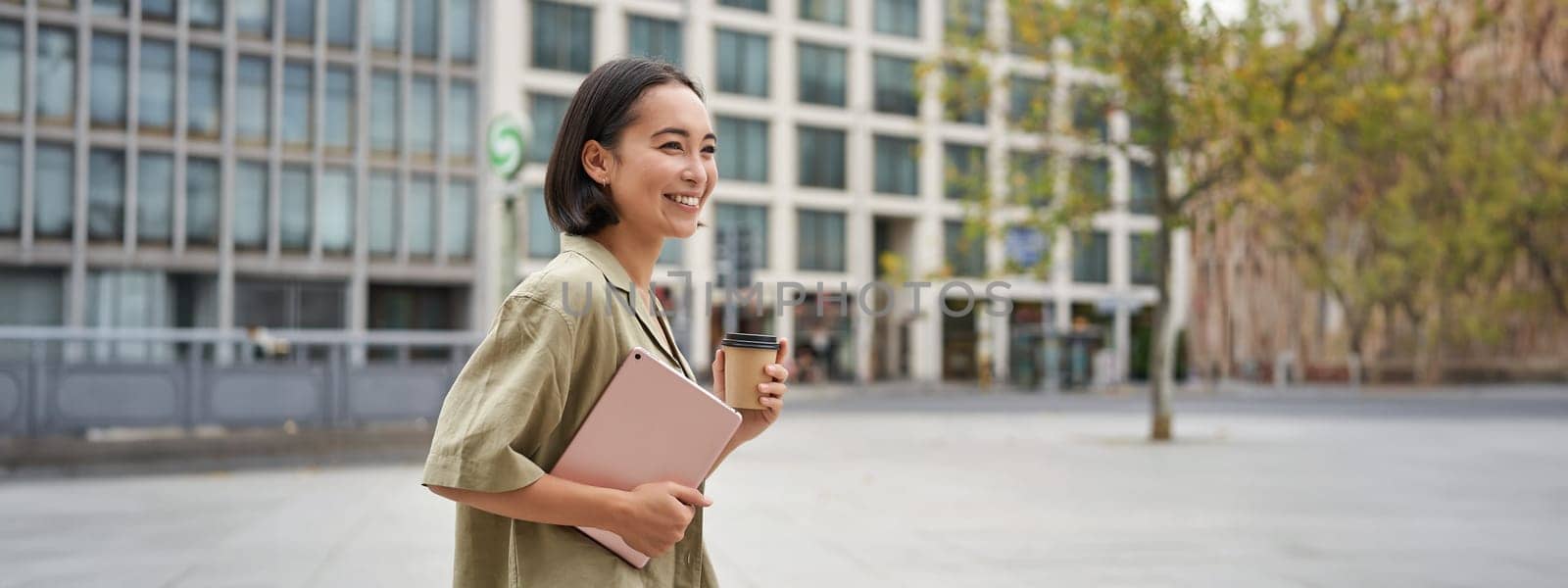 Stylish city girl with tablet, walking on street and drinking takeaway coffee, going to university or work.