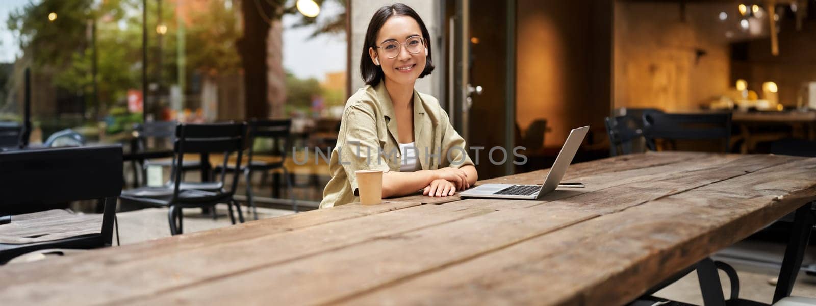 Portrait of asian girl in glasses, sitting with laptop in cafe, working remotely, studying online, posing with coffee and computer.