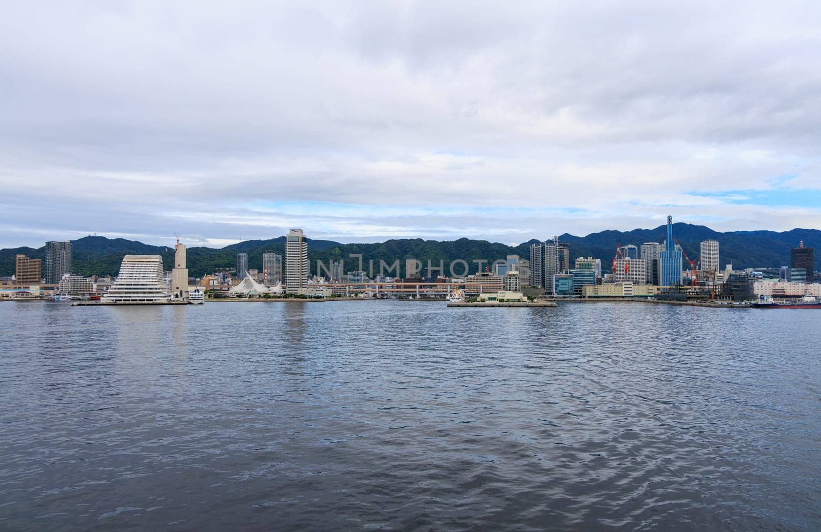 Kobe, Japan - September 23, 2023: View from water of Kobe City and harbor on cloudy day by Osaze