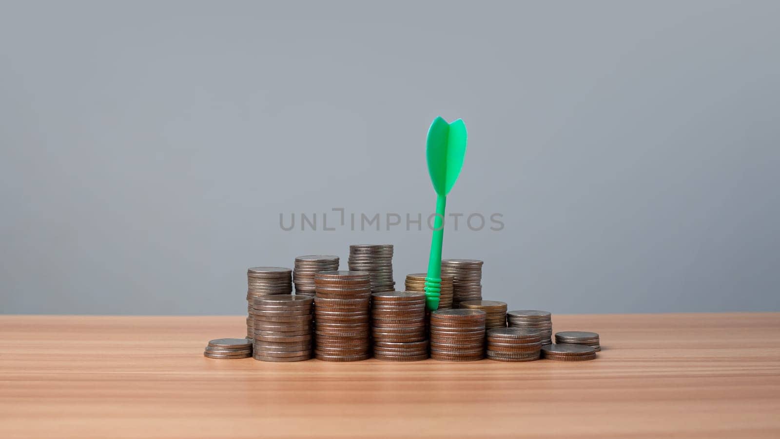 The green arrow hits the target in the center of a row of coins on the wooden floor. Concepts of finance, savings and investment. Business growth concept, finance goals concept.