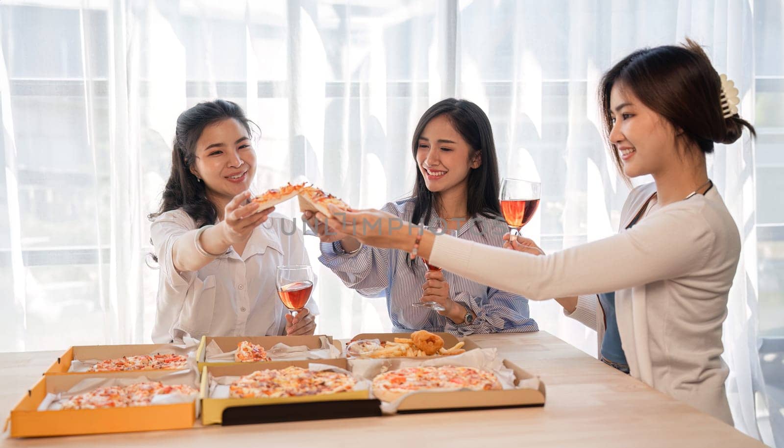 Group of Asian friends together to celebrate Christmas with champagne and eating pizza at home. Joy of holiday party with friends or colleague concept by wichayada