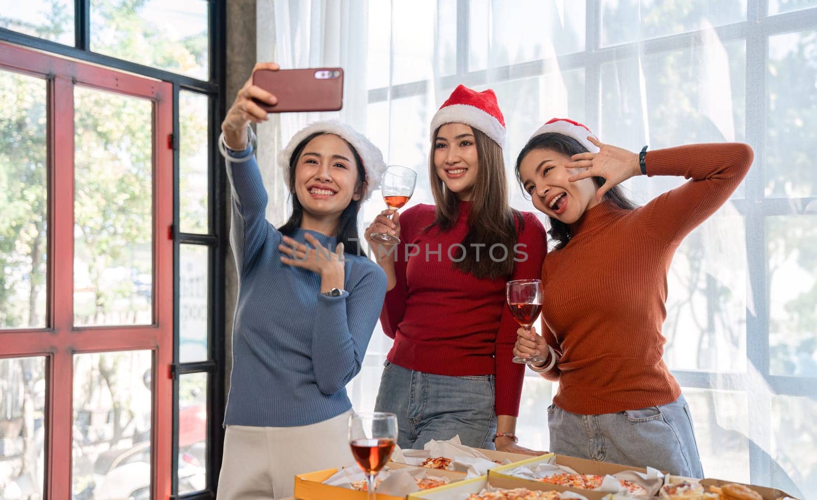 Group of Asian friends together to celebrate Christmas with champagne and eating pizza at home. Joy of holiday party with friends or colleague concept by wichayada