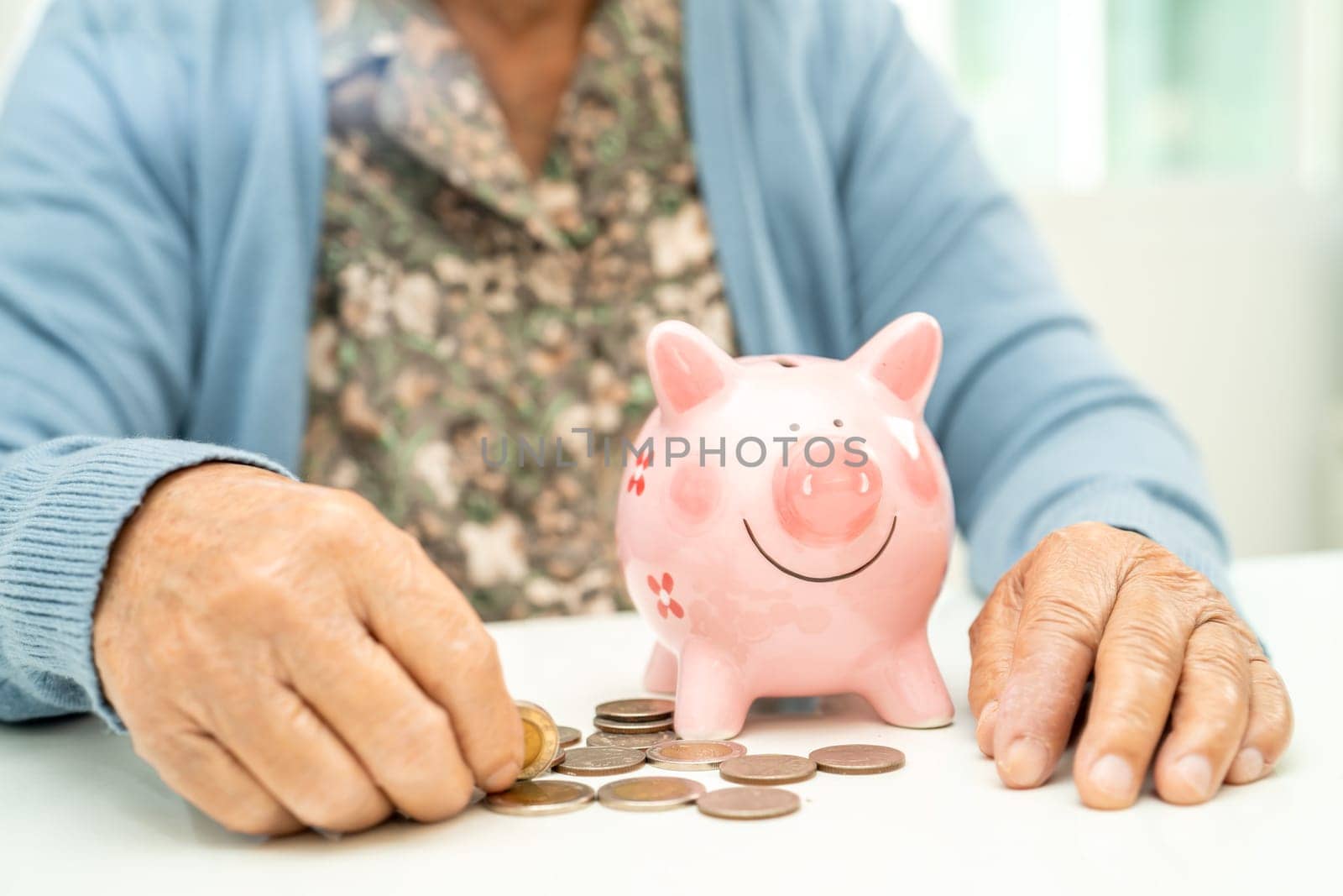 Asian elderly woman putting coin into pink piggy bank for saving money and insurance, poverty, financial problem in retirement. by pamai