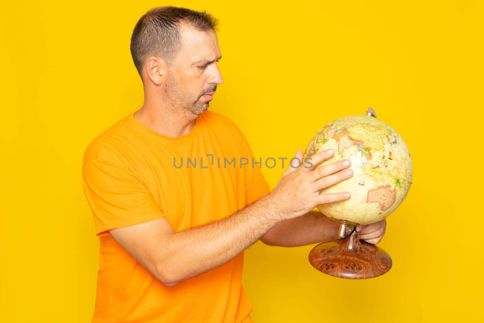Hispanic man with beard in his 40s searching for a location on a world globe, isolated on yellow background. by Barriolo82