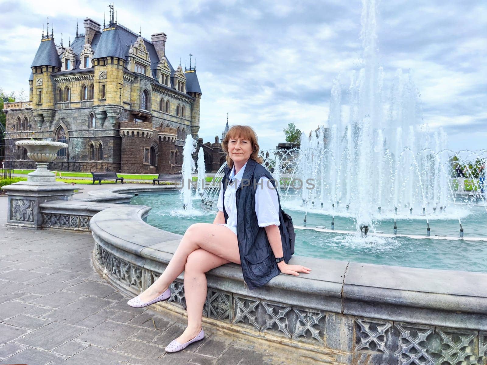 A woman enjoys her travel adventure at Garibaldi Castle, showcasing her excitement in a historic setting. The adventures of a middle-aged female tourist on a trip