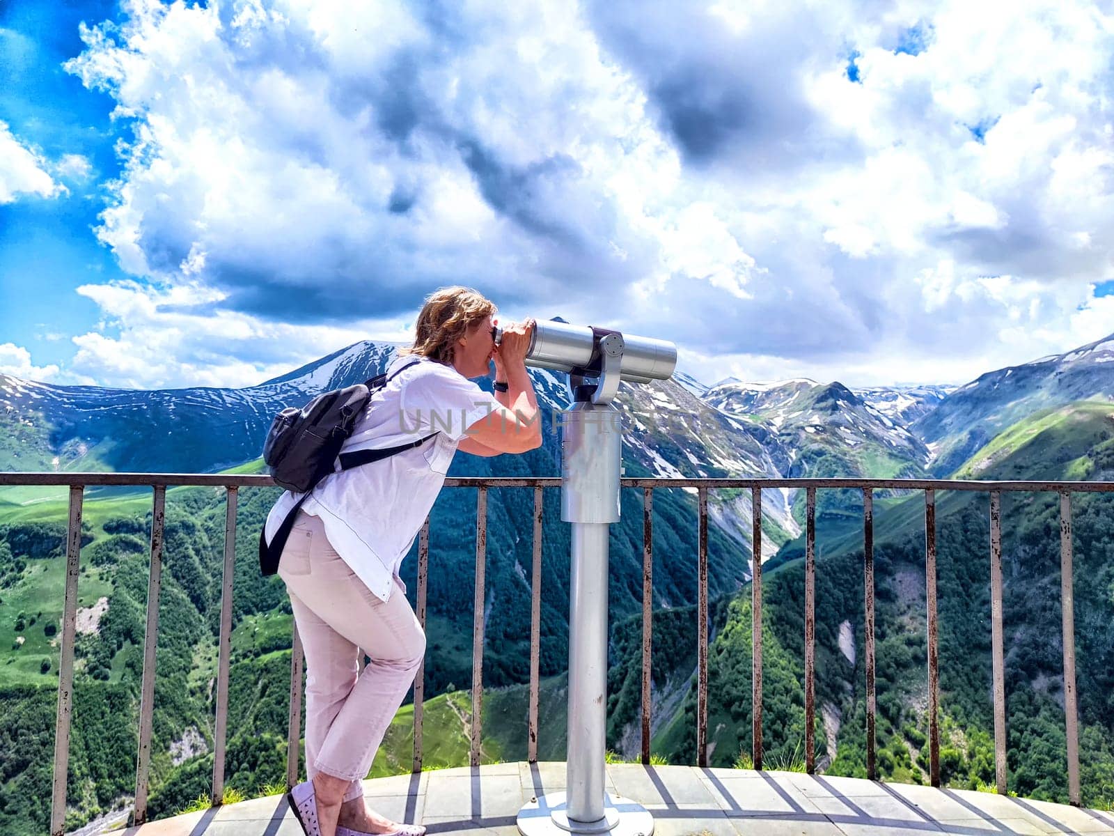A woman is gracefully standing on a beautiful balcony that overlooks a stunning mountain range, enjoying the breathtaking view ahead