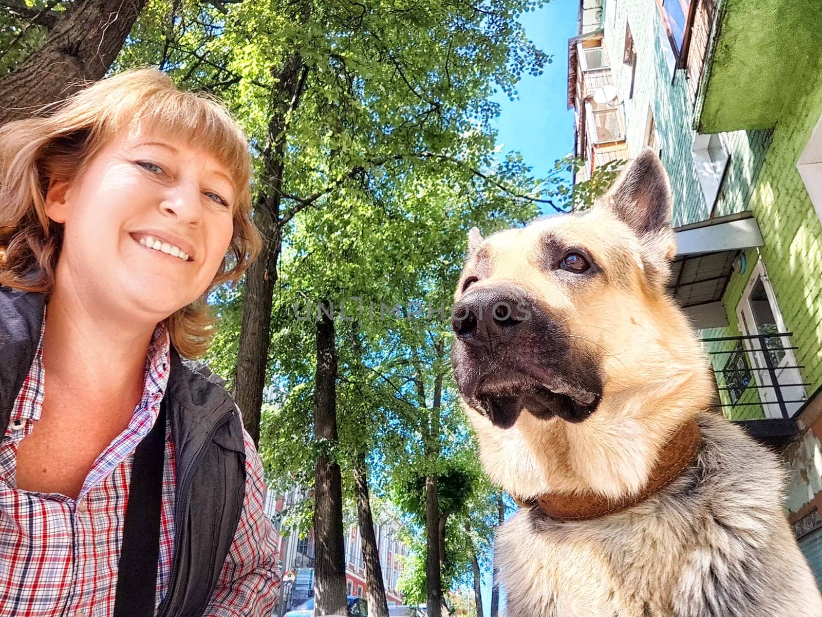 A woman is cheerfully posing for a picture alongside a friendly German Shepherd dog, capturing a joyful moment together in the frame