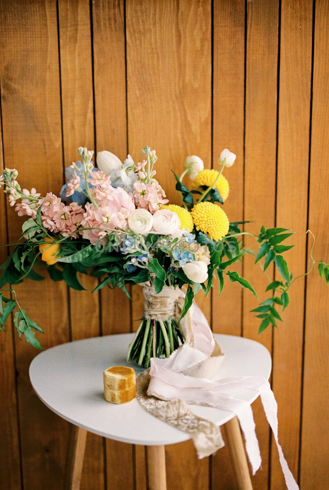 Bride bouquet stands on a white chair near a box with rings against a wooden wall. High quality photo