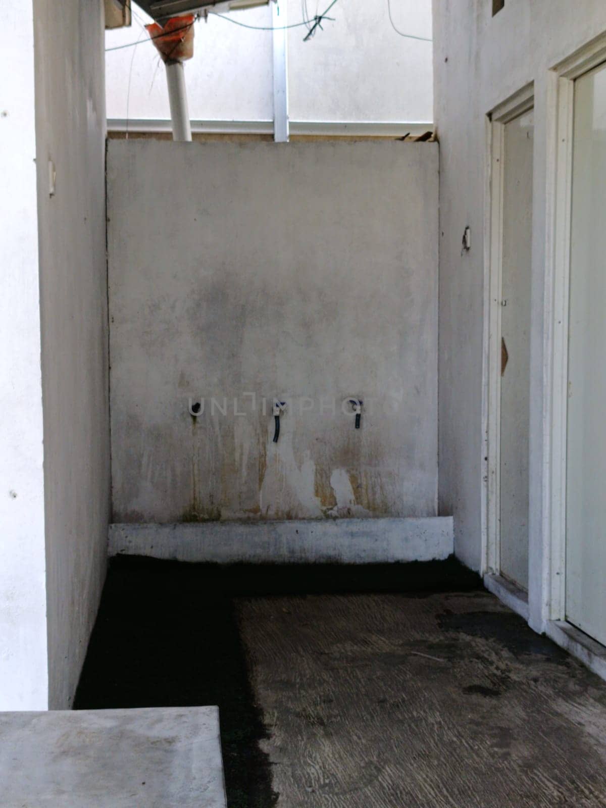 An old, neglected washroom with stained concrete walls and worn faucets. The image conveys a sense of abandonment and decay, portraying a stark, utilitarian environment.