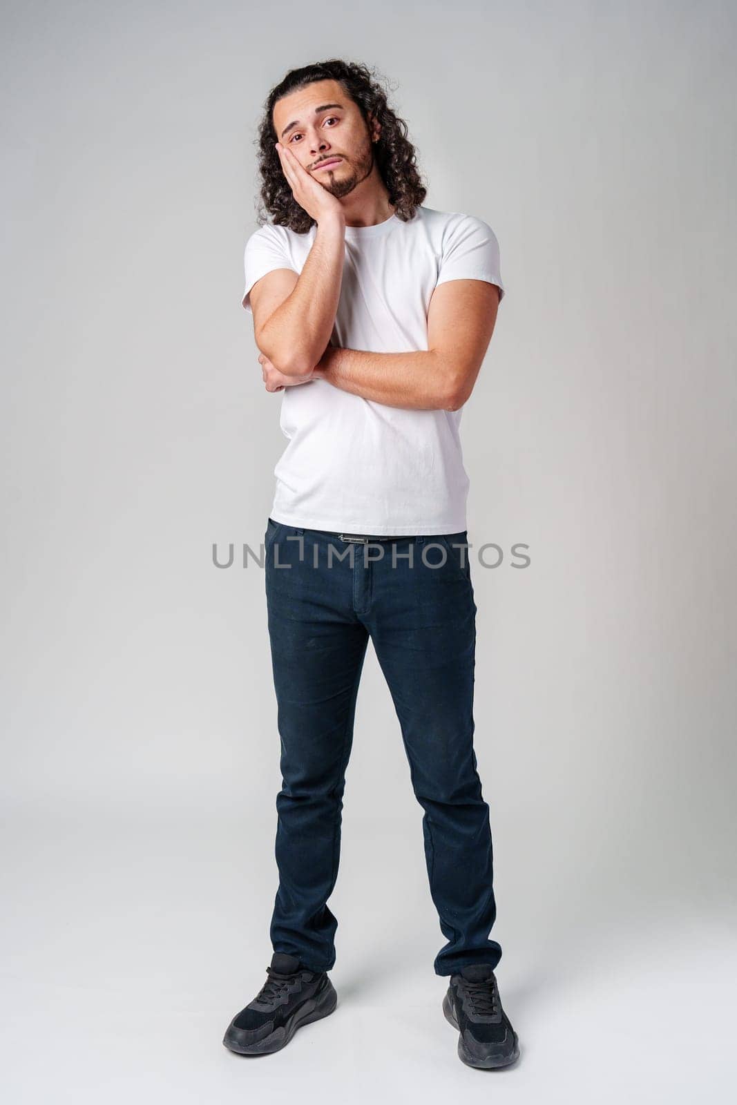 A young man stands thoughtfully against a plain background, expressing contemplation close up